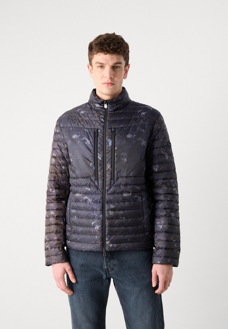 Pikowana kurtka puchowa w ciemnym granacie z subtelnymi szarymi wzorami, wysoki kołnierz, zamek błyskawiczny oraz dwie przednie kieszenie z czarnymi suwakami.