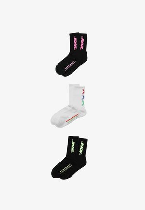 Tres pares de calcetines para tripulación: negros con texto rosa, blancos con chevrones rojos, azules y verdes y texto, y negros con texto amarillo pálido, extendidos planos.