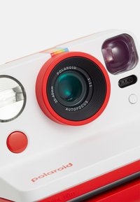 Polaroid camera with white and red casing, featuring a circular black autofocus lens, integrated flash, and a red button on the front.