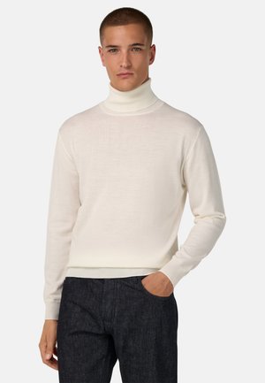 Cremfarbener Rollkragenpullover mit langen Ärmeln, gerippten Bündchen und Saum. Getragen mit dunkelblauen Denim-Hosen, die eine glatte Textur und eine taillierte Passform aufweisen.