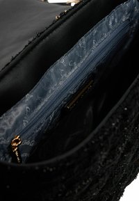 Zwarte handtasinterieur met een gladde textuur. Voorzien van een vak met rits en een blauwe voering met subtiel patroon. Gouden hardware-accenten.