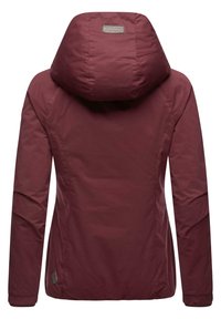 Bordowa kurtka z kapturem o gładkiej, matowej fakturze, z szwami i metką na górnej części pleców. Lekka i zaprojektowana z myślą o użytkowaniu na zewnątrz.