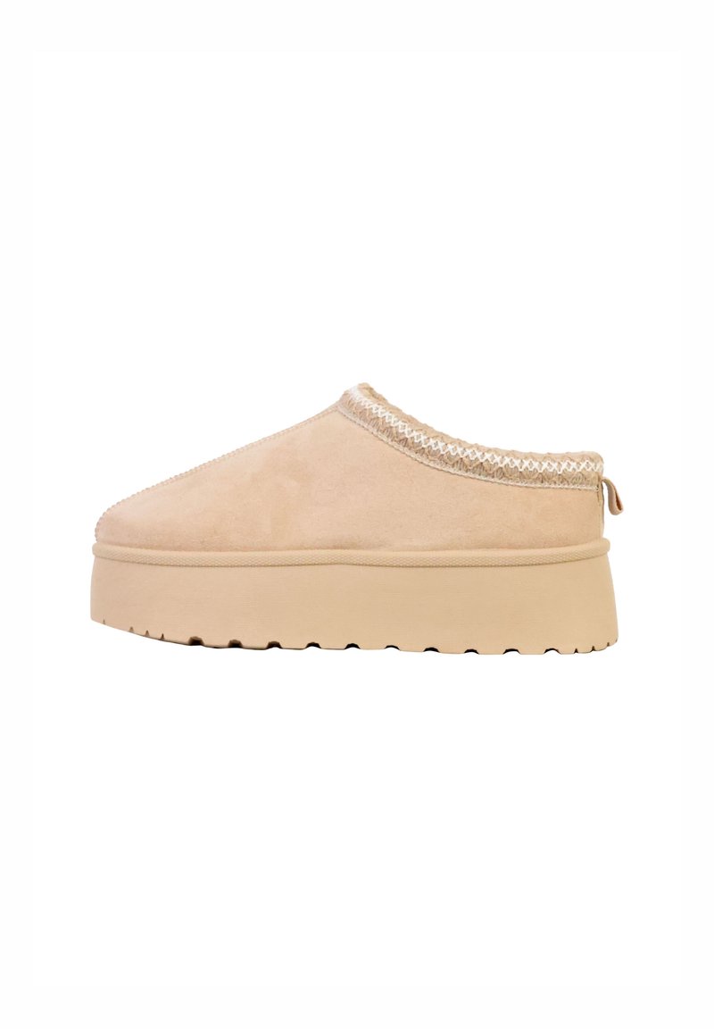 Beige ruskindssko med slip-on design, tekstureret kant, plateau-sål og diskrete dekorative syninger rundt om kraven. Flad gummisål.
