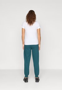 White short-sleeve t-shirt paired with teal joggers. The joggers have an elastic waistband and cuffs, worn with black sneakers.