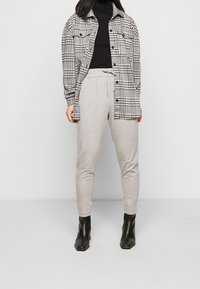 Zwart-wit geblokte shirtsjas over een zwarte coltrui, gecombineerd met grijze tapered sweatpants en zwarte enkellaarsjes.