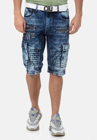 Denim-Cargo-Shorts in einer verblassten blauen Waschung, mit mehreren Zip-Taschen, strukturierten Akzenten und einem weißen Gürtel mit einer markierten Schnalle.