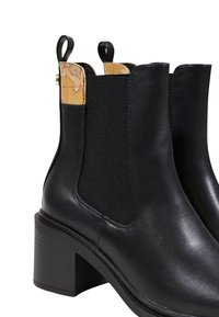 Botines de piel negra con paneles laterales elásticos, acentos texturizados en beige en la parte superior y un tacón cuadrado. Acabado suave con detalles mínimos.