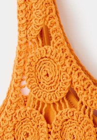 Tissu crochet orange avec des motifs circulaires et tressés complexes superposés sur un fond textile orange uni.
