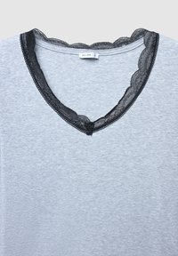 Top grigio con scollatura a V in pizzo nero ondulato. Il tessuto presenta una fine trama a coste, aggiungendo un dettagliato sottile al design complessivo.