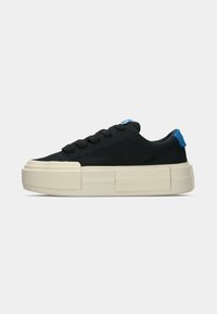 Scarpe da ginnastica nere in suede con suola spessa di colore crema, con un dettaglio blu sul tallone e lacci neri. Design minimalista.