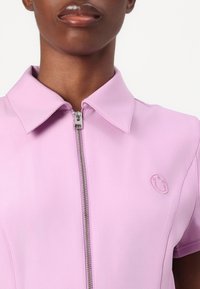 Roosa lukuga polo särk, millel on krae, lühikesed varrukad, tekstureeritud kangas ja rindkeres väike broderi naeratuse logo.