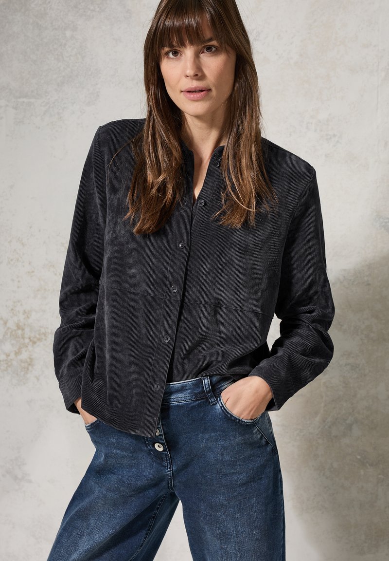 Black corduroy shirt with a button-down front, featuring a collared neck and long sleeves, paired with blue denim jeans.
