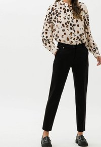 Lepelprint blouse in crèmewit, met knopen en een mandarin col; zwarte, op maat gemaakte broek met een gladde textuur; chunky zwarte schoenen.