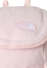 Light pink backpack with a soft fleece flap, featuring a white embroidered logo. The body is crafted from durable fabric, unique in texture.
