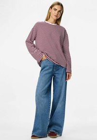 Červeno-bíle pruhovaná košile s dlouhým rukávem a volným střihem, nošena s světle modrými širokými džínami a bordó botami. Jednoduchý a ležérní outfit.