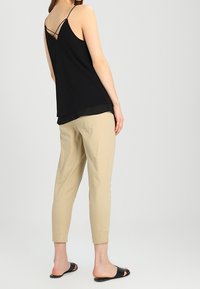 Svart ärmlös topp med tunna band och lagerdesign; matchad med ljusbeige tapered byxor och svarta slidesandaler.