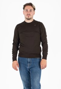 Pull à manches longues côtelé marron foncé avec un col ras du cou et des poignets ajustés. Présente un petit logo sur la partie supérieure gauche de la poitrine.
