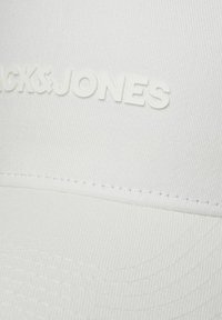 Hvid baseballhat med tekstureret stof og forhøjet hvid "BLACK & JONES" logo på fronten, med glat rund skygge og syninger som accent.