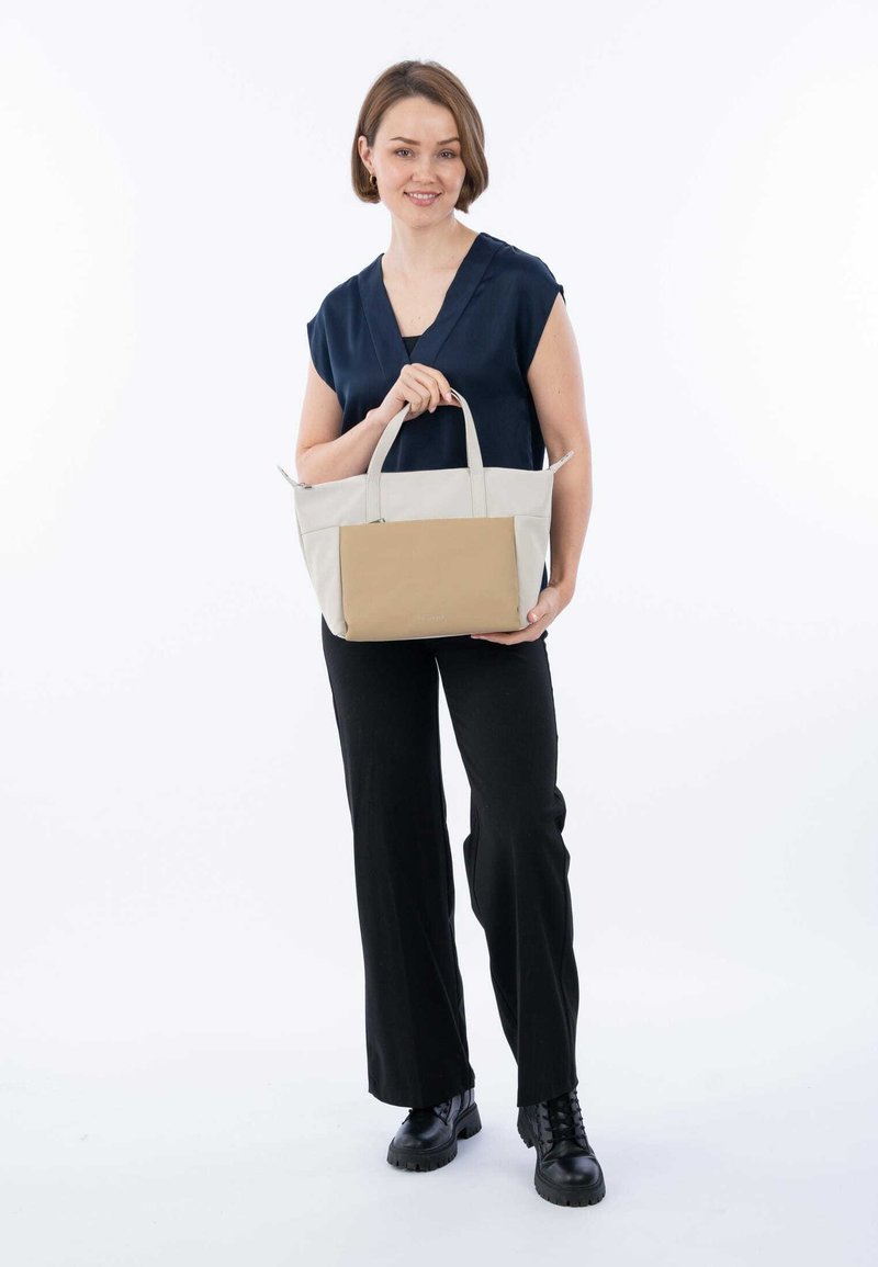 Bolso tote con secciones en color crema y marrón claro, que presenta asas dobles y una forma rectangular. El material parece suave con un diseño estructurado.