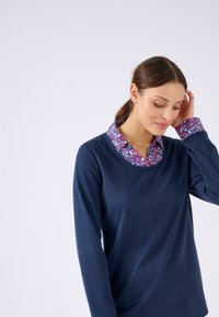 Haut à manches longues bleu foncé avec un col et des poignets à motif floral. Texture douce et coupe ajustée. Remarque : le col présente des détails floraux vibrants en rose et violet.