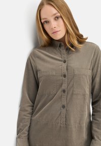 Chemise verte olive à boutons en tissu texturé avec deux poches poitrine, dotée d'un col classique et d'une base droite.