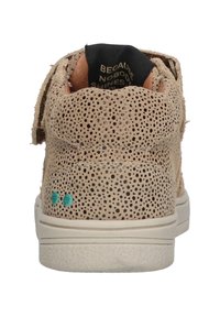 Zapatillas de cuero beige con textura perforada, suela de goma blanca y acentos en turquesa. La vista trasera muestra el logo en el forro interior.