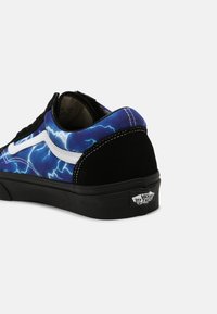 Baskets Vans bleues et noires avec motif d'éclair blanc, bande latérale blanche, semelle noire et logo "Vans Off The Wall" au talon.