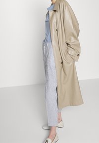 Beige läder trench coat, ljusblå skjorta, randiga byxor och vita loafers. Kappan har en oversized passform och stora knappar.