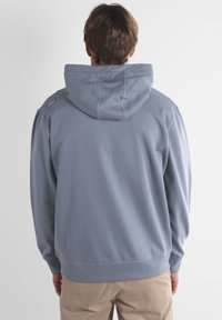 Sweatshirt gris avec capuche, poignets côtelés et taille élastique, présentant une texture lisse et des détails de couture subtils.
