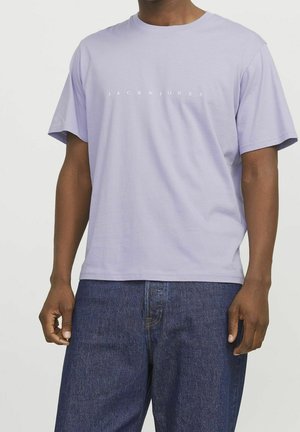 Jasnofioletowa bawełniana koszulka z krótkim rękawem, z centralnie umieszczonym białym napisem "JACK & JONES" na wysokości klatki piersiowej.