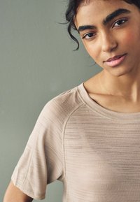 Camisa de manga corta en un suave tejido texturizado de color beige claro, con cuello redondo y detalles de costura visibles.