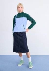 Ljusblå och grön fleecepullover med hög krage, två zipparade sidofickor, tillsammans med en mörk denimkjol och gröna sneakers.