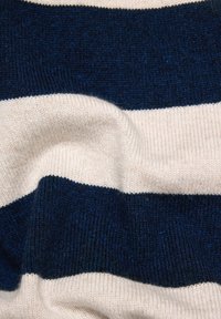 Gestrickter Pulloverstoff mit abwechselnden marineblauen und cremefarbenen Streifen, der eine weiche Textur mit einem gerippten Abschluss an den Kanten zeigt.