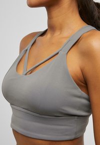 Gray sports bra featuring crisscross straps, a fitted silhouette, and smooth fabric texture. Designed for active wear with minimal seams.