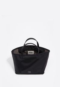 Melnā soma ar divām rokturiem, kas izgatavota no gludas auduma, ar rāvējslēdzēja aizdari un redzamu iekšējo etiķeti ar zīmola nosaukumu.