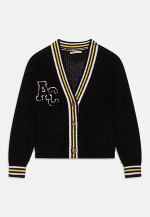 Cardigan en maille noire avec col en V, trois boutons marron, bordure rayée blanche et jaune, et écusson "AC" sur la poitrine gauche.