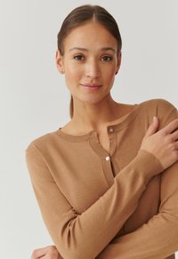 Bruine gebreide cardigan met een ronde hals, lange mouwen en knoopsluiting. Zachte textuur en slim-fit ontwerp. Eenvoudige, effen kleur.