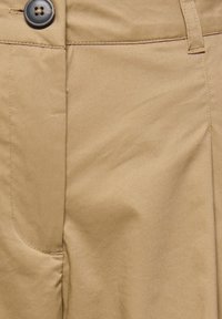 Gros plan d'un pantalon beige avec une poche avant visible, des coutures cousues et un bouton marron foncé à la taille.