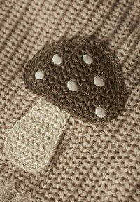 Virkat textil med ett brunt svampmönster med vita prickar på en beige bakgrund. Texturerad tyg med ett vävt mönster.
