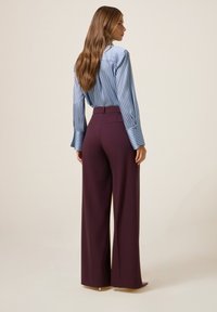 Modrá a bílá pruhovaná blůza s dlouhými rukávy a zadním yoke, spárovaná s kalhotami v burgundské barvě s vysokým pasem a širokými nohavicemi.