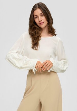 Witte blouse met lange, gestructureerde mouwen en geplooide manchetten, gecombineerd met beige hoog waaiende broeken met een knoopdetail.