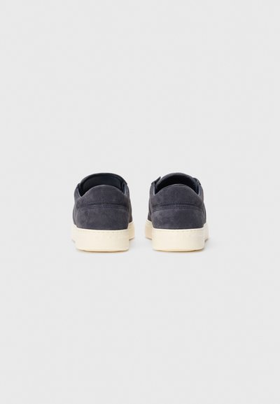 Pair of dark blue suede sneakers with off-white rubber soles viewed from the back against a plain light background.