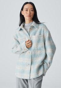 Veste en laine rayée bleu clair et blanche avec un devant boutonné, deux poches poitrine et une coupe décontractée. Texture douce remarquable.