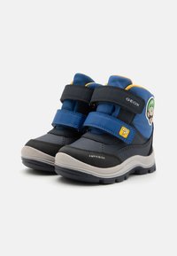Bottes pour enfants à la cheville en bleu et noir. Elles comportent deux bandes auto-agrippantes, une semelle en caoutchouc et un graphique d'un personnage avec un point d'interrogation.