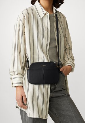 Schwarze, texturierte Leder-Umhängetasche mit einem Reißverschluss, ausgestattet mit einer Fronttasche und goldenen Hardware-Details, kombiniert mit einem gestreiften Shirt.