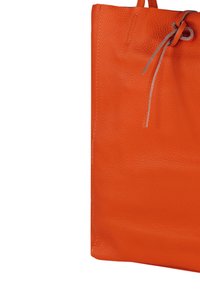 Tote bag van feloranje leer met een gestructureerd oppervlak, voorzien van een trekkoordsluiting en subtiele stikdetails langs de randen.