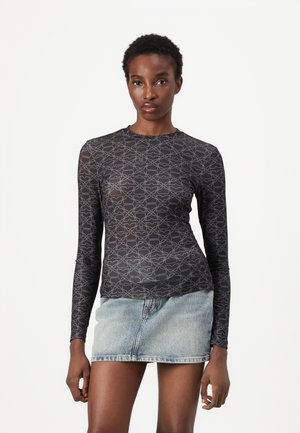 Long-sleeve black top featuring a tonal geometric pattern, made of a sleek material, paired with a light denim mini skirt.