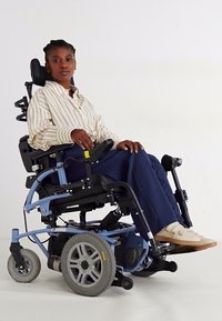 Elektrinė neįgaliojo vežimėlis su mėlynu rėmu, dideliais pilkais ratais, reguliuojamais sėdynėmis ir valdymo pultu. Vartotojas vilki dryžuotą marškinėlį ir tamsias kelnes.