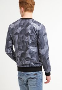Sweatshirt gris à motif géométrique en tissu doux, avec un col rond et des poignets noirs aux manches et à la taille.