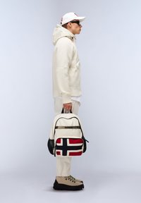 Zaino con motivo della bandiera norvegese, presenta un tessuto cremoso testurizzato, dettagli neri e una maniglia superiore. Il modello indossa un abito beige.